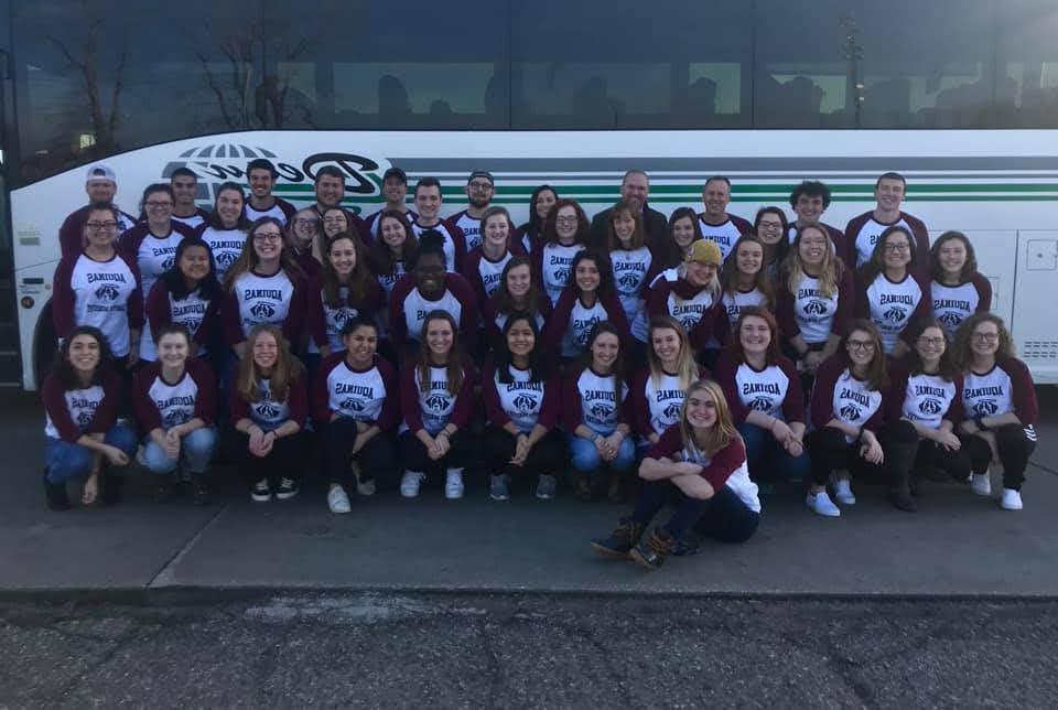 Large group of students wearing matching T-shirts in front of a large bus
