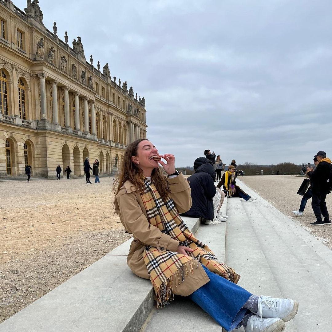 Student eating a macaron on the steps of a castle or palace.
